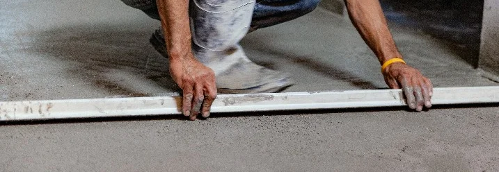 Person ebnet Betonboden mit Richtlatte